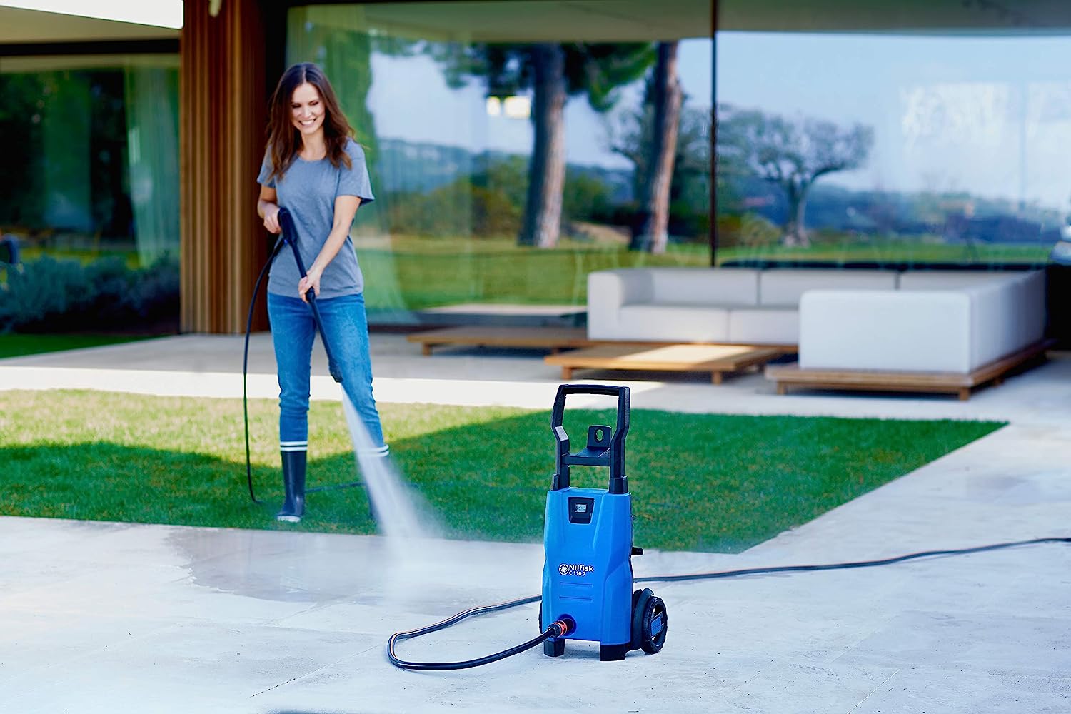 Woman cleaning her patio with a Nilfisk domestic pressure washer, efficiently removing dirt and grime for a refreshed outdoor space