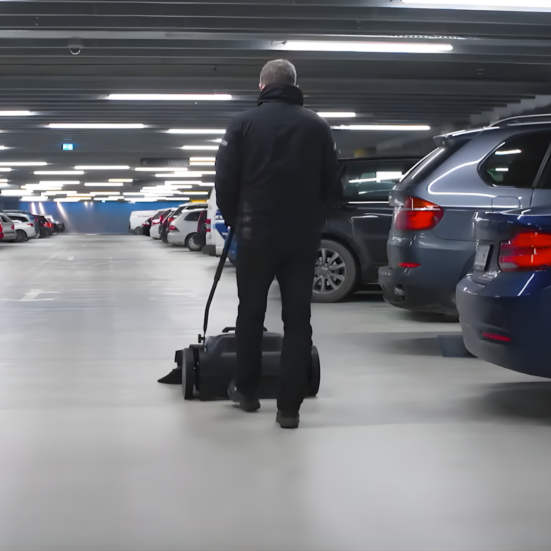 Operator using Nilfisk SW250 manual push sweeper to clean debris from car park floor