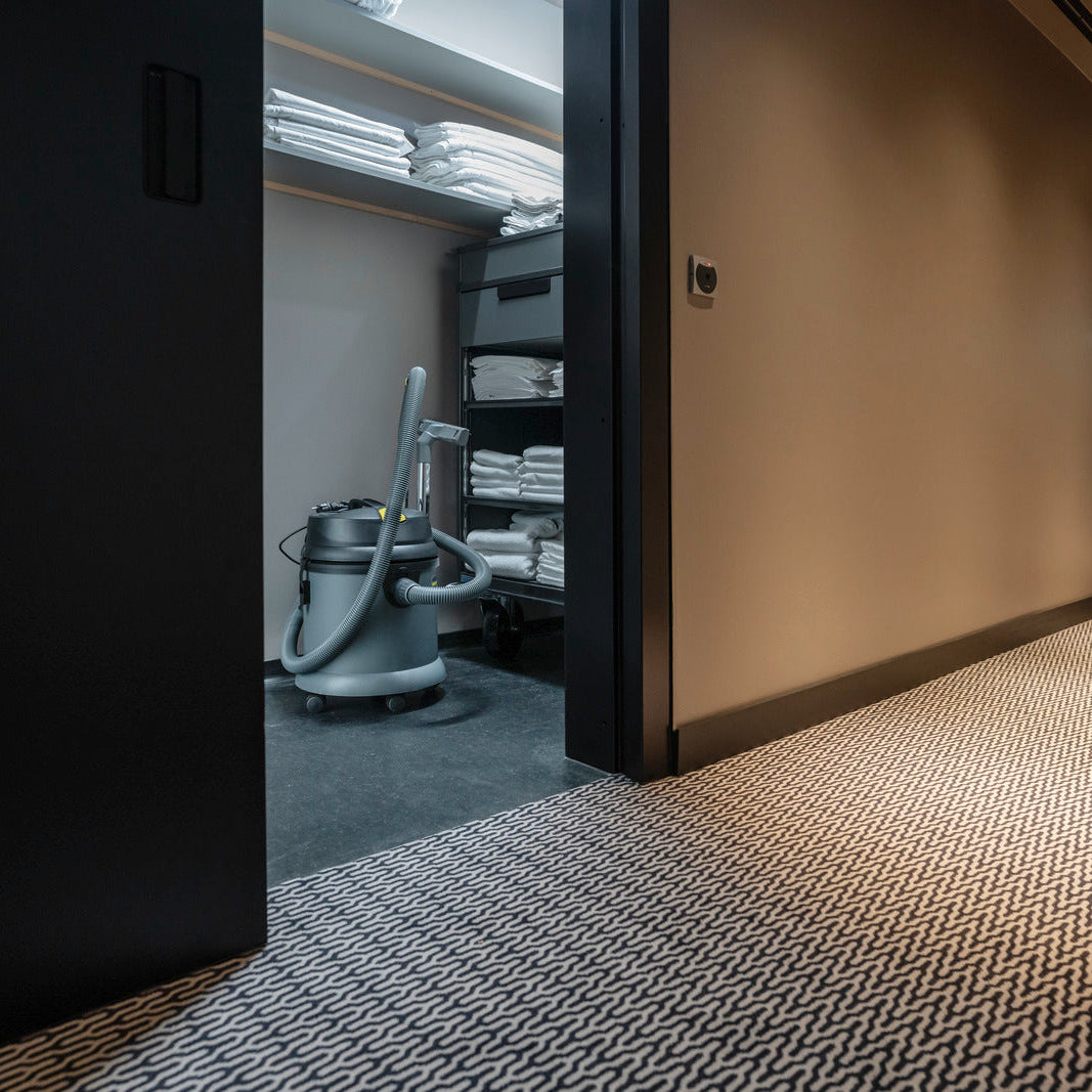 Janitor storage closet with wet and dry vacuum, trolley, and stacked towels in hotel hallway
