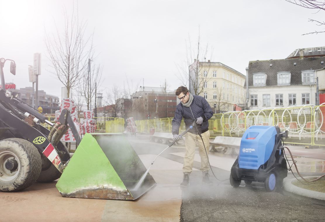 Man using Nilfisk Hot Pressure Washer to clean tractor bucket - Industrial Equipment Cleaning