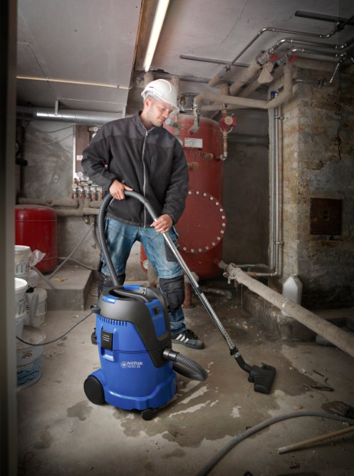 Operator using Nilfisk AERO 26-21 wet and dry vacuum in industrial workshop