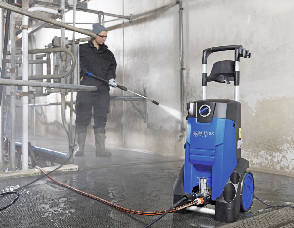 Operator using Nilfisk MC3C 150/570 XT pressure washer for heavy-duty cleaning in an industrial environment
