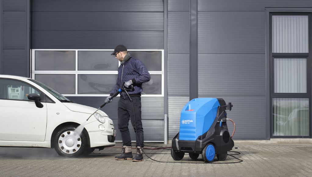 Operator using Nilfisk MH3C industrial hot pressure washer for outdoor cleaning of commercial surfaces