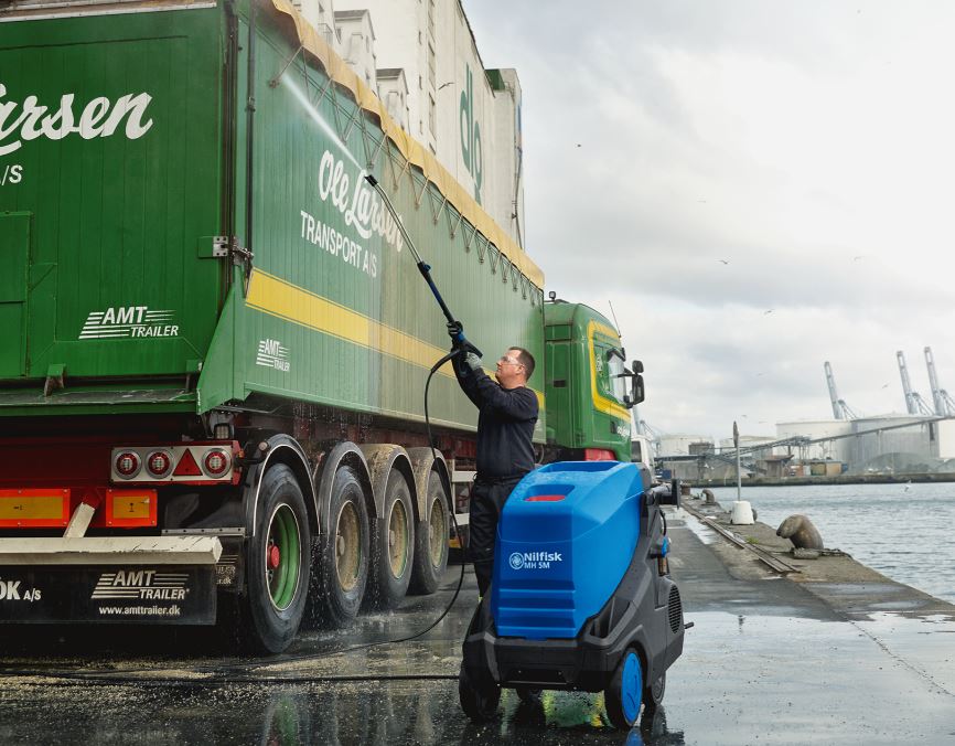 Operator using Nilfisk MH5M hot pressure washer to clean a commercial truck exterior