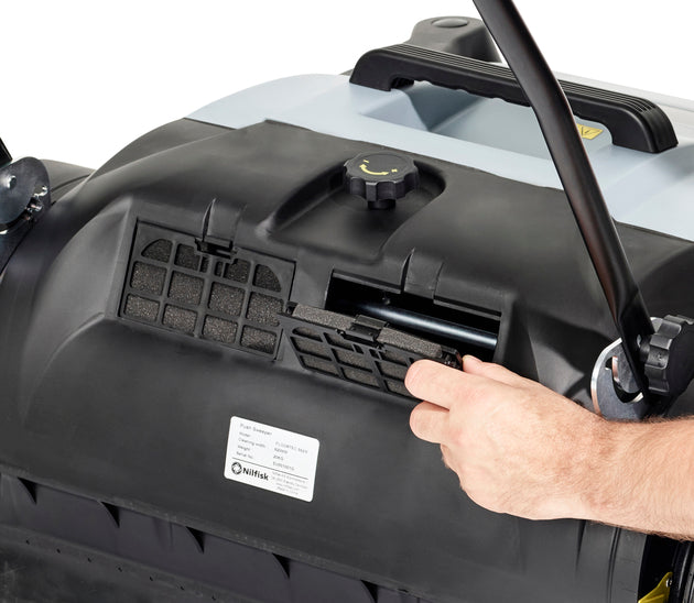 Operator emptying debris container from Nilfisk SW250 push sweeper after cleaning session