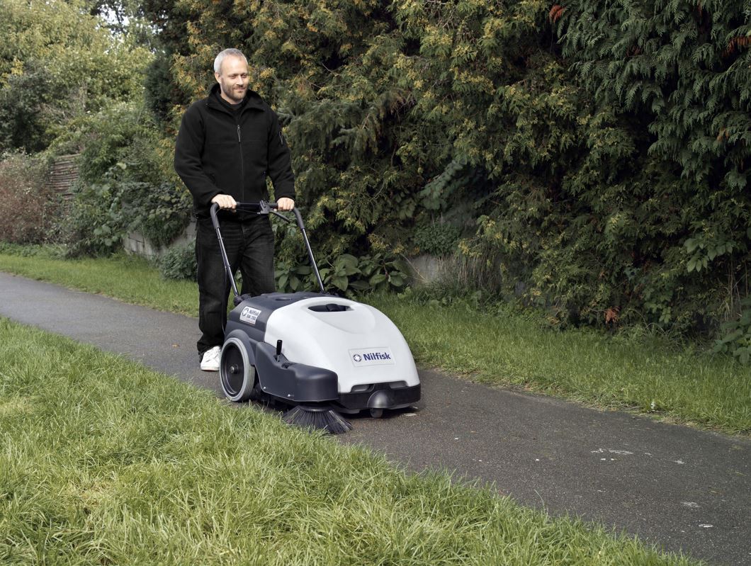 Nilfisk SW750 battery floor sweeper in use outdoors on concrete surface near grass edge