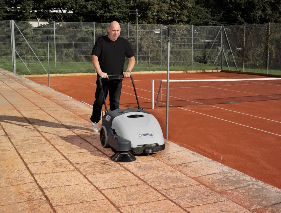 Operator using Nilfisk SW750 electric floor sweeper to clean outdoor walkway or sports area